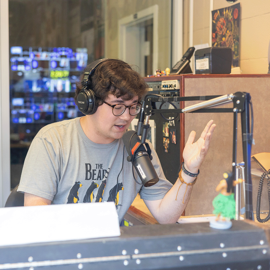 Student talks into a microphone in a radio booth.
