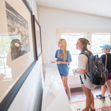 Three women look at framed photos on wall