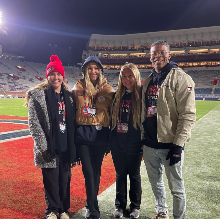 Four students smile while standing on a football field.