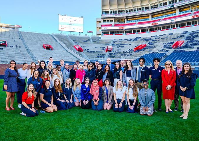 Group of students and guests pose for a photo on the football field.