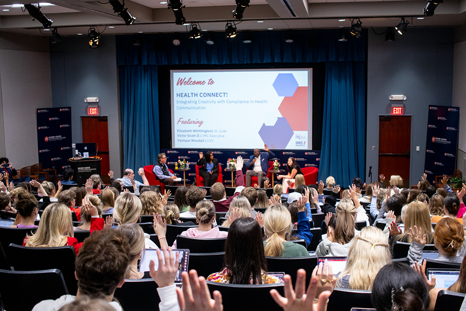 A lecture hall full of students raise their hand.