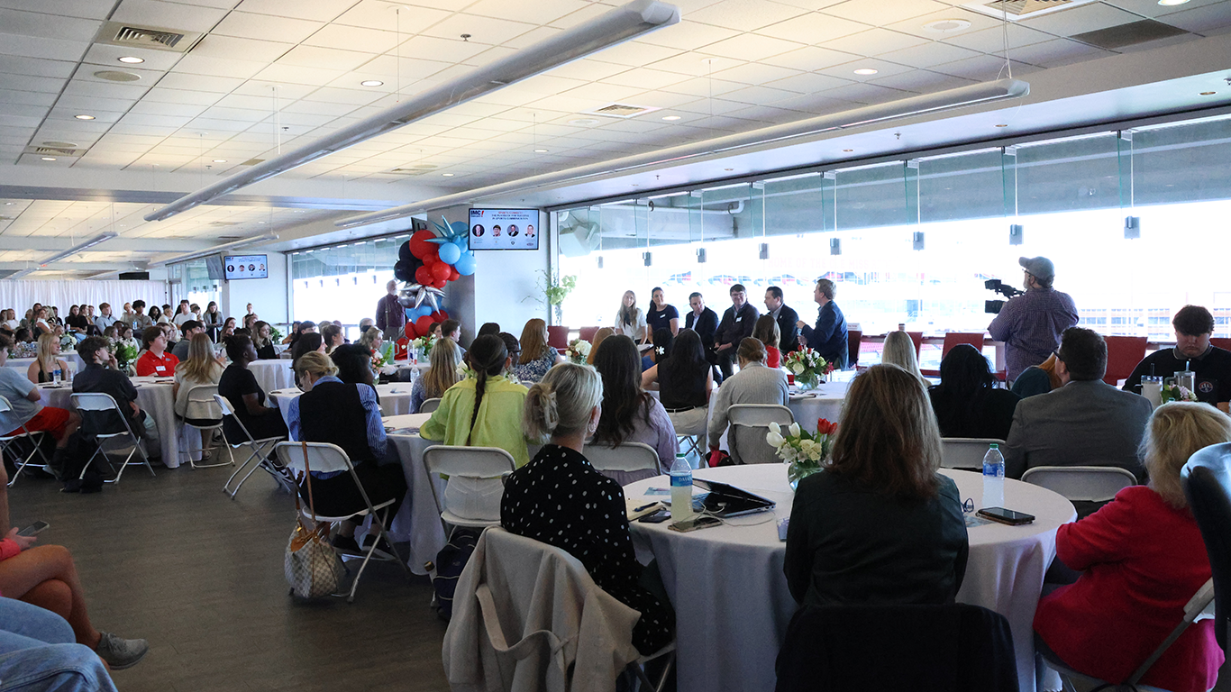 Speakers talk to a large room of guests overlooking a football field.