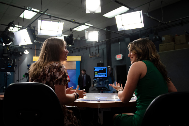 Two news anchors talk to each other.