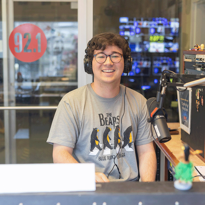 Student smiles for a photo while sitting in a radio booth.