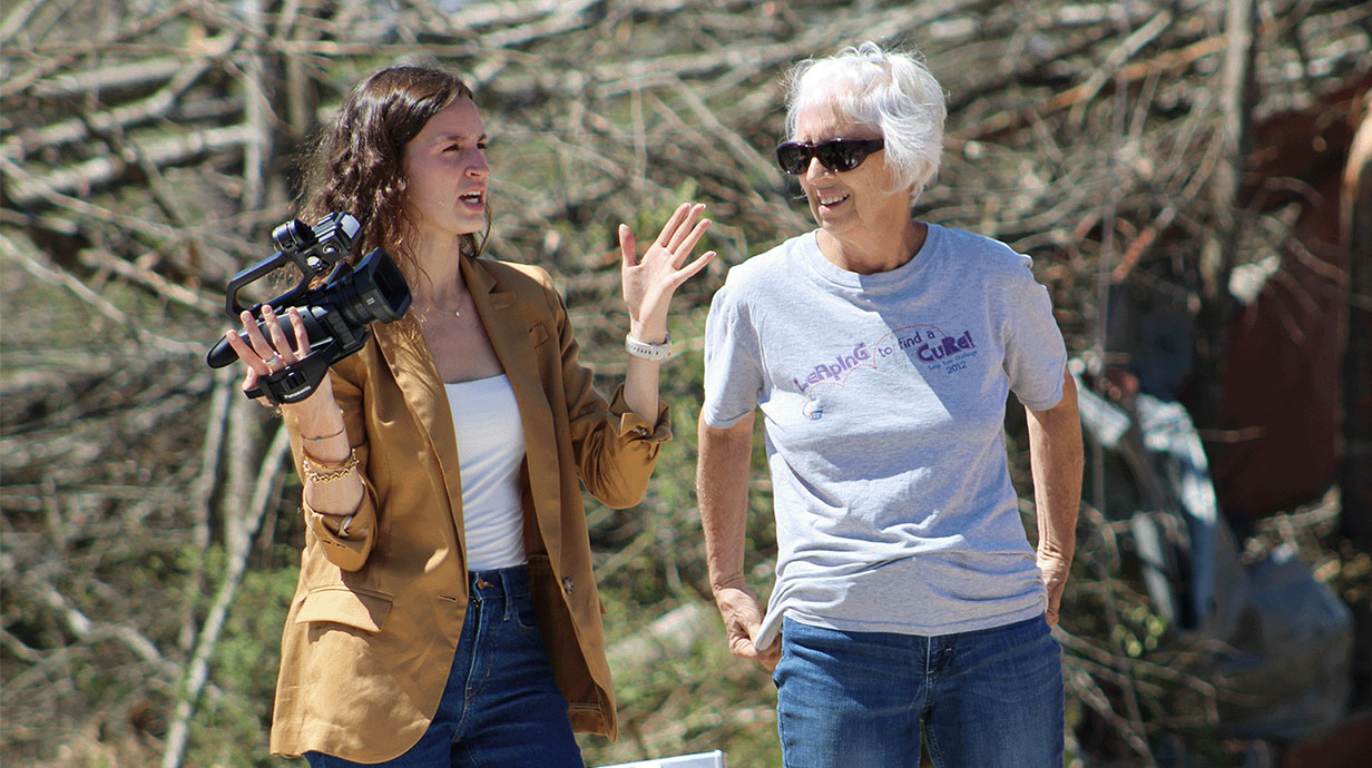 Student carries a camera while talking to a woman.