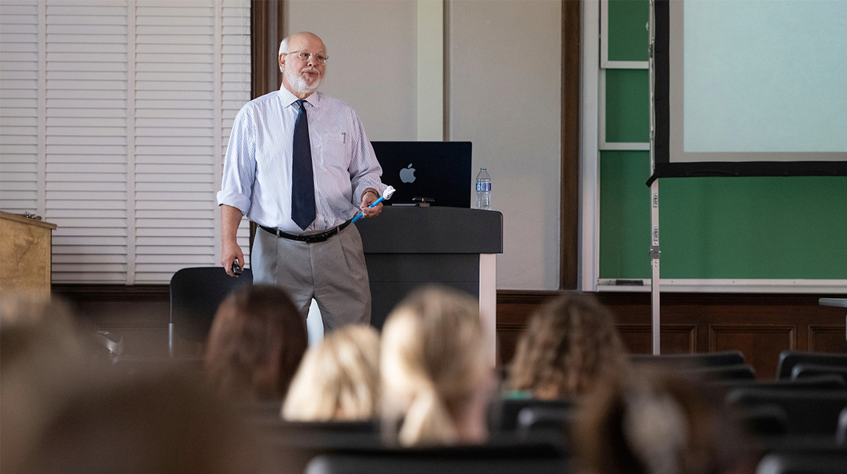 A professor stands at the front of an auditorium and talks to students.